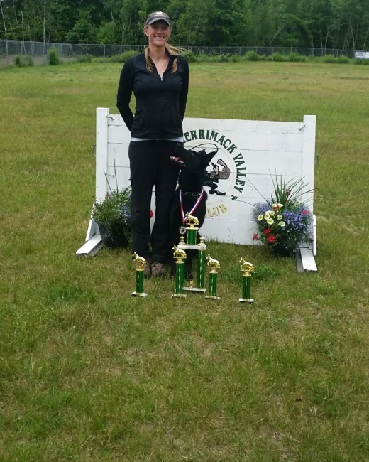 A handler with a German Shepherd and trophies at a working-dog competition